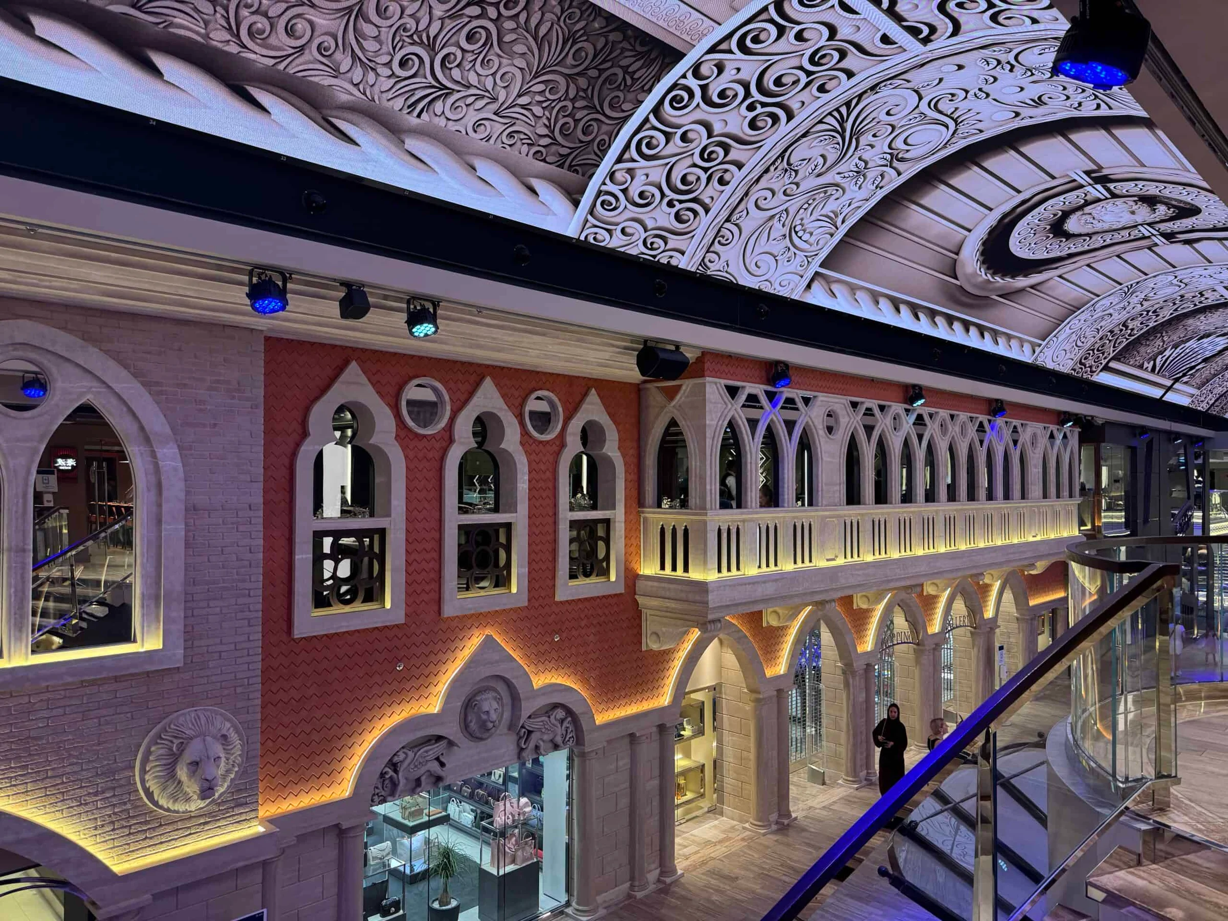 Ornate interior atrium of a cruise ship with Venetian-style arches, red brick walls and an elaborately carved ceiling.