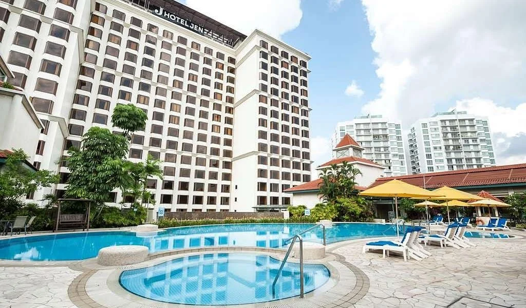 Hotel Jen sign on a tall white hotel building behind an outdoor swimming pool with sun loungers and yellow umbrellas