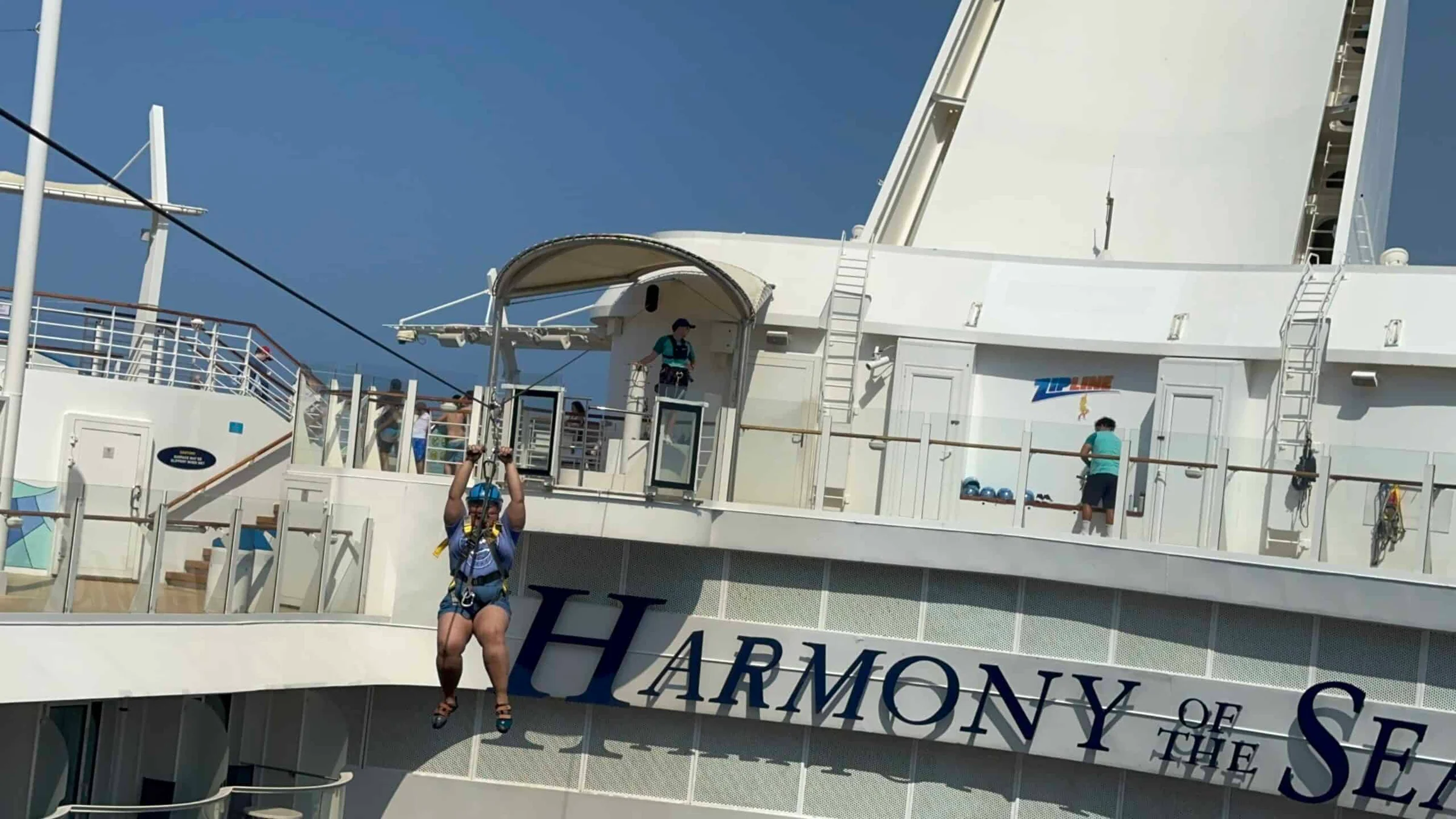 A person in a harness rides a zip line along the side of the Harmony of the Seas cruise ship.