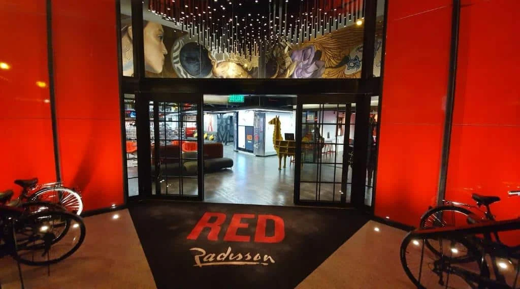 The entrance to Radisson RED hotel with red walls, a branded doormat, and bicycles on either side.