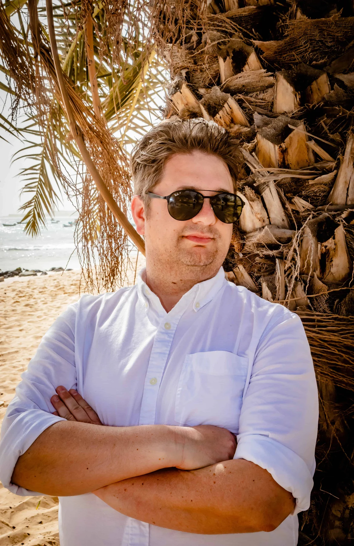 Ben on a beach beside a palm tree