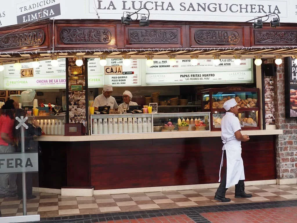 La Lucha Sangucheria open-fronted food counter with staff in white uniforms serving customers