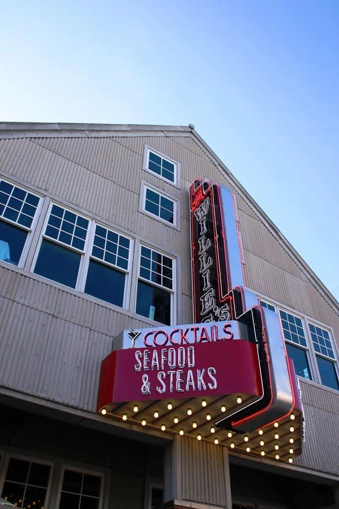 Low-angle view of Willie's Cocktails Seafood and Steaks restaurant sign with marquee bulb lights on a pale building facade.