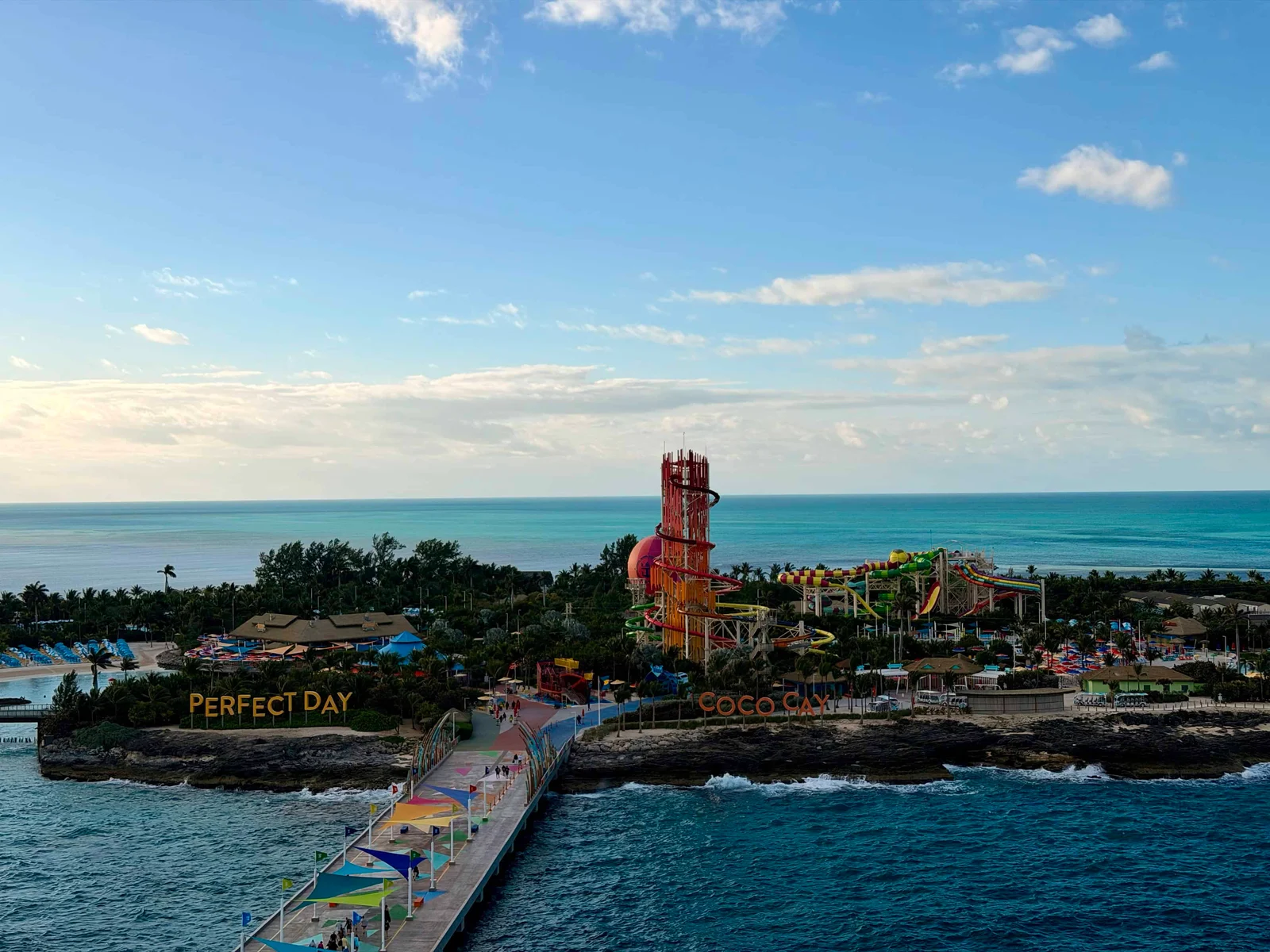 A colourful waterpark island with a tall slide tower, trees and a pier, with signs reading Perfect Day and Coco Cay.