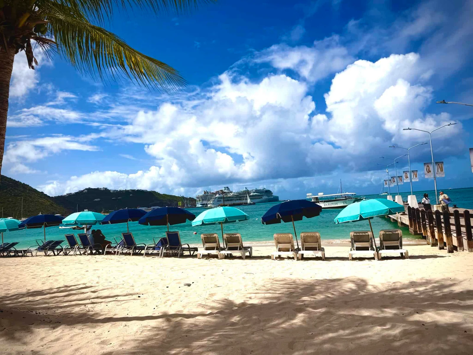 Beautiful tropical beach with sun loungers, umbrellas, and a cruise ship in the background.