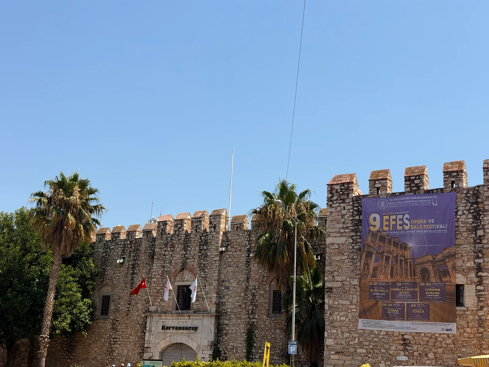 A stone castle with battlements displays a festival banner, with palm trees and a Turkish flag visible nearby.