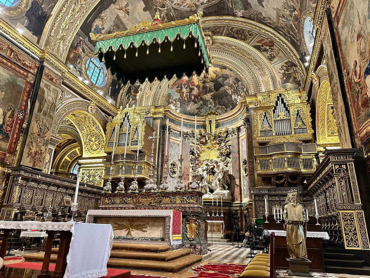 Ornate gilded cathedral interior with a marble altar, painted ceiling, pipe organs and carved wooden choir stalls.