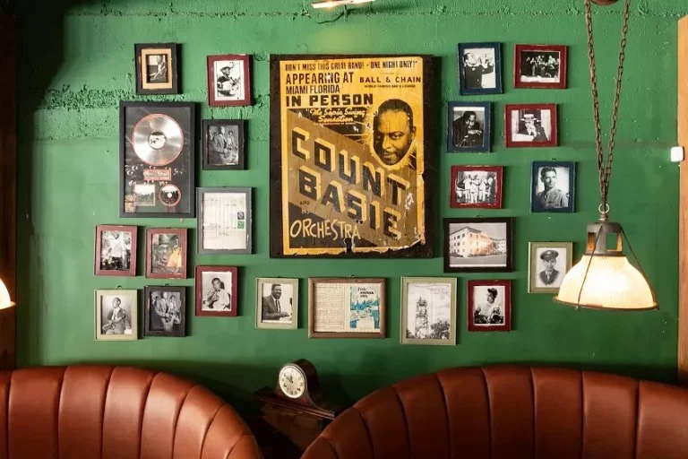 Green wall covered in framed black and white photos and a vintage Count Basie Orchestra concert poster above a brown leather booth seat.