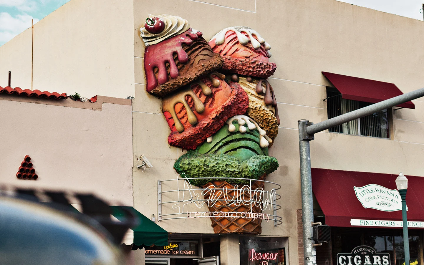 A large colourful sculptured ice cream cone sign on the exterior wall of Azucar Ice Cream Company next to a cigar shop.