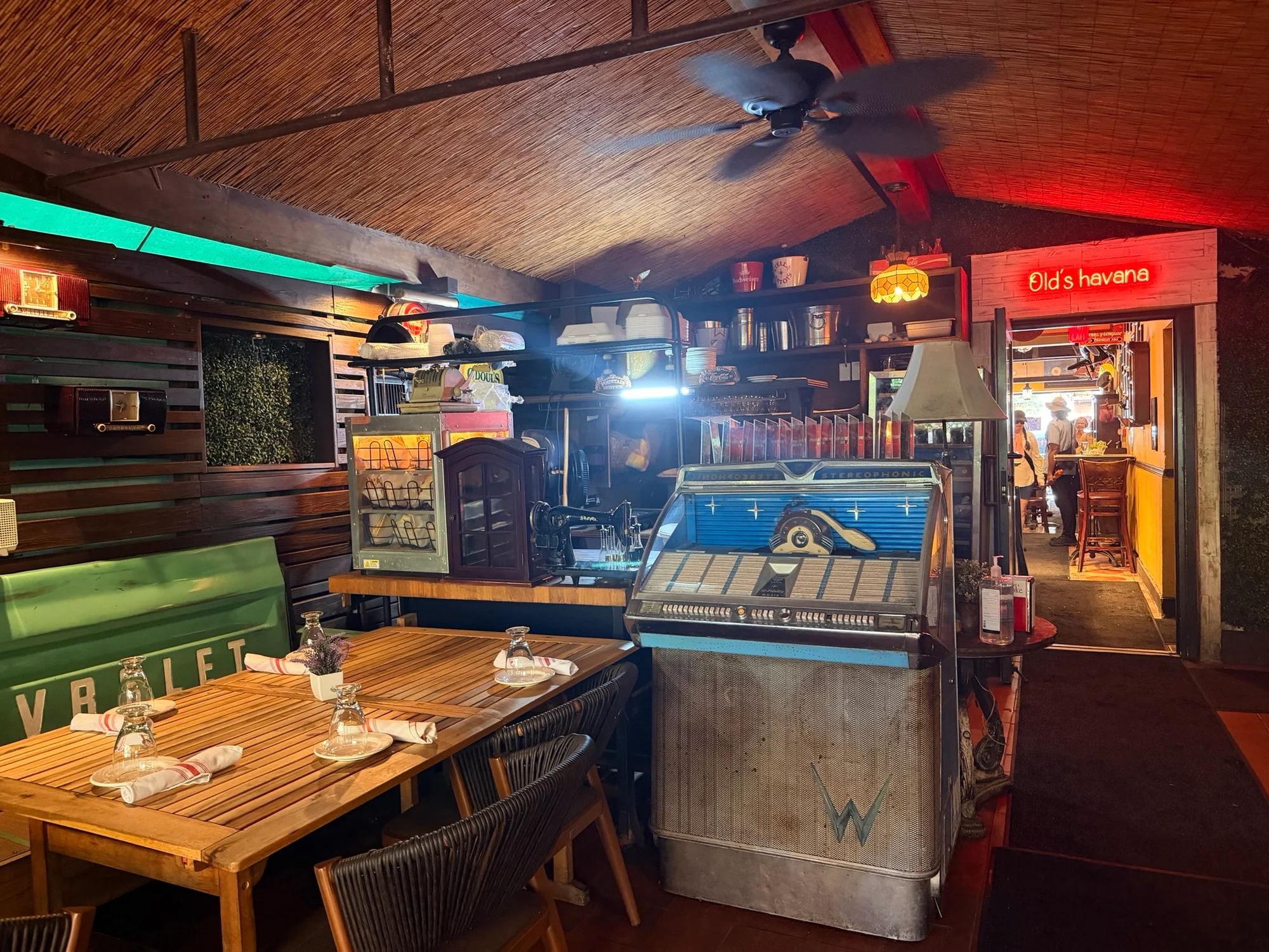 A rustic bar interior with wooden tables, a vintage jukebox and an Old's Havana neon sign above a doorway.
