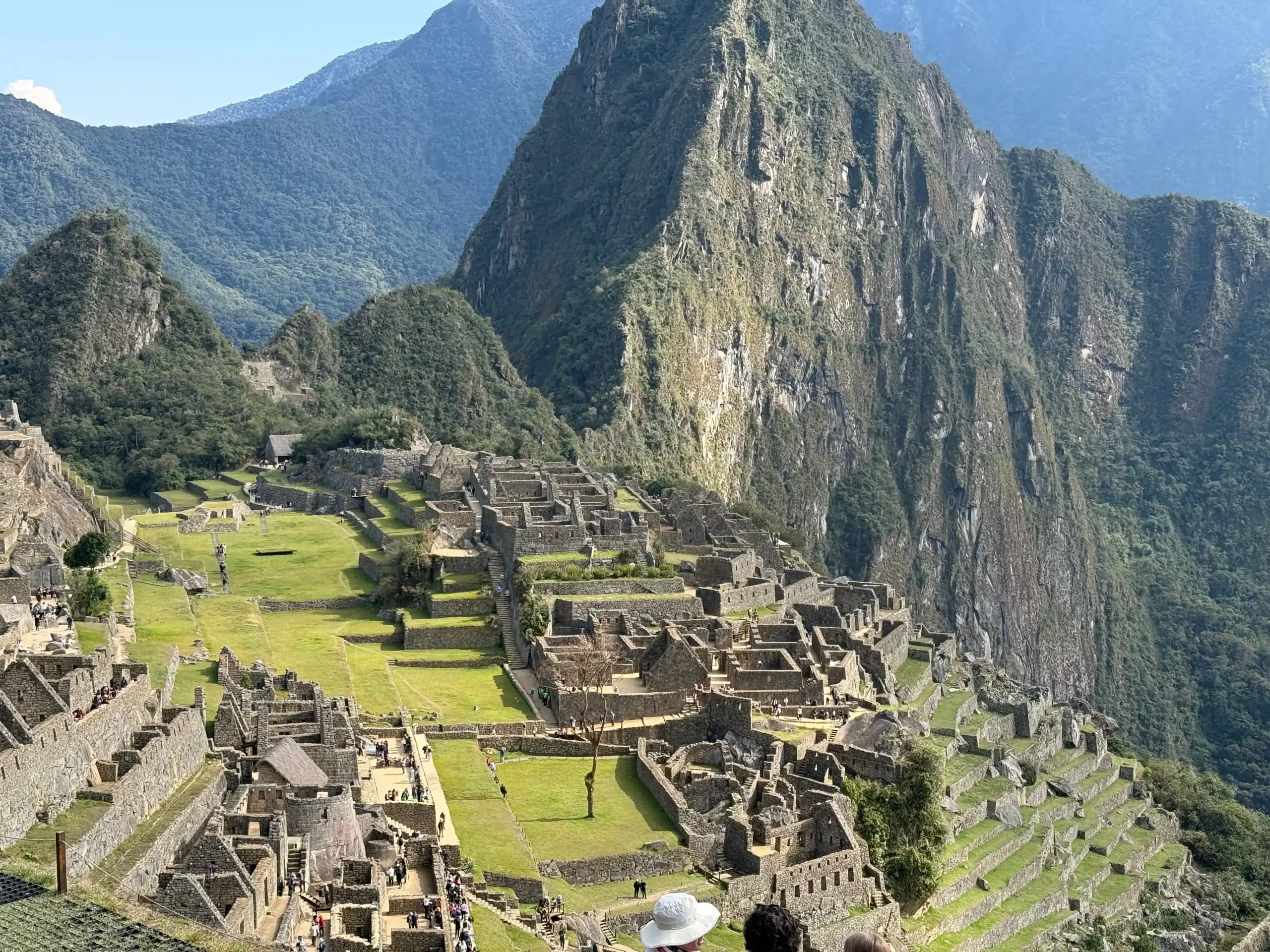 View of Machu Picchu’s ancient stone ruins and terraces set against steep green mountains under a clear sky.