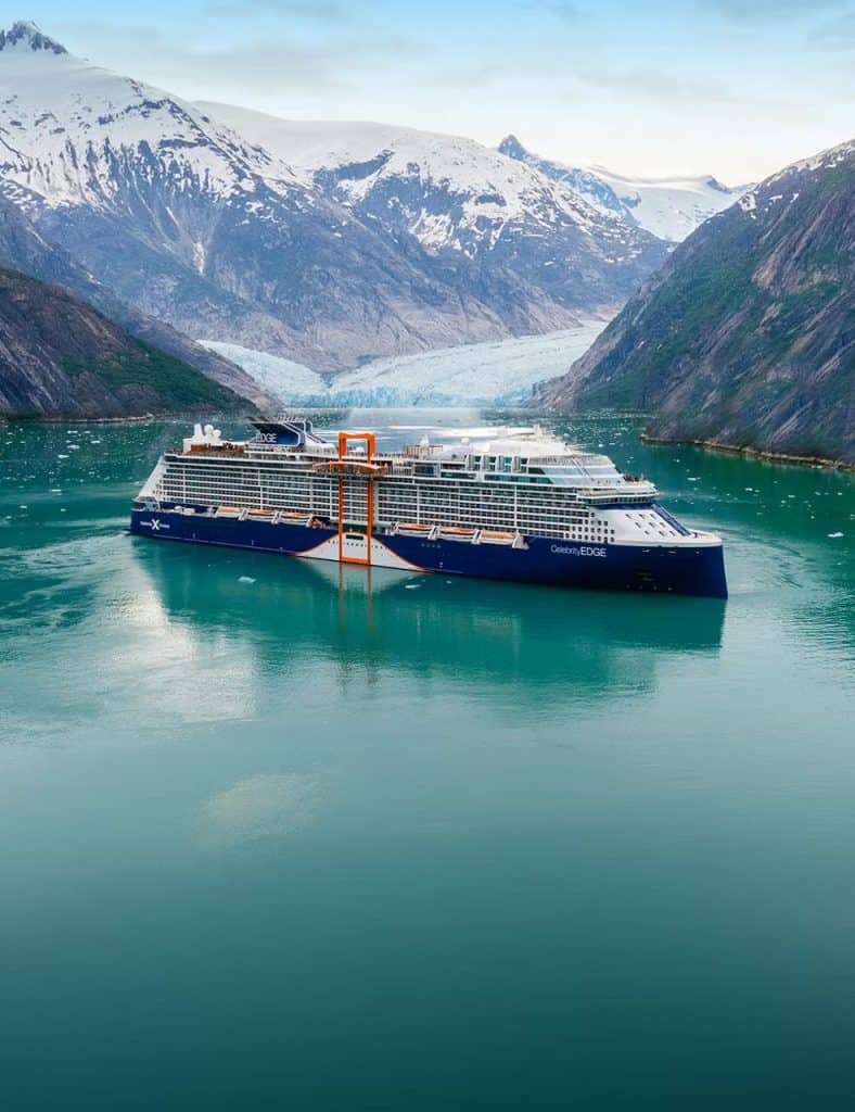Luxury cruise ship sailing through a scenic fjord with snow-capped mountains.
