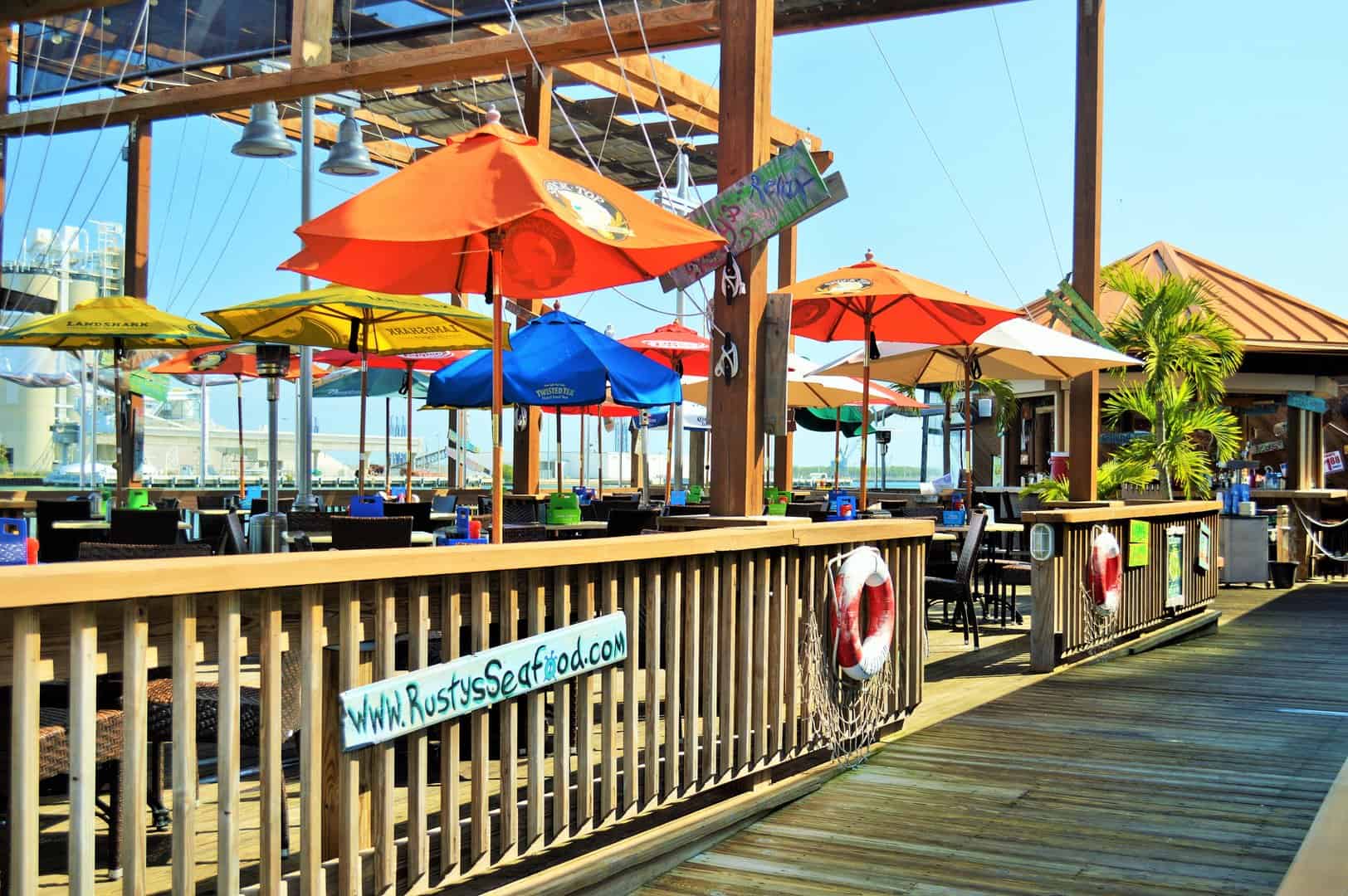 Outdoor dining area at Rusty's Seafood & Oyster Bar with colourful umbrellas and waterfront views.
